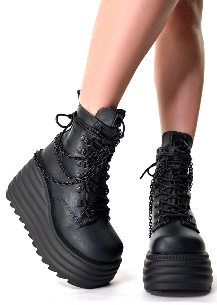 Demonia MORTE 65 Black Rave Platform Boots in black vegan leather with metal chain drape and 4.5 inch wedge platform worn by model — front view