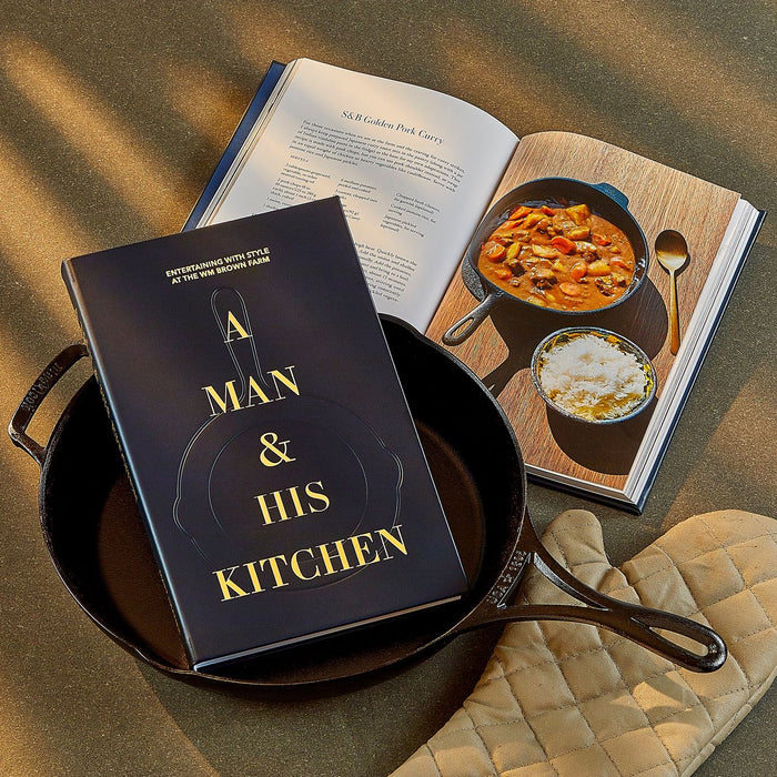 Cookbook titled 'A Man & His Kitchen' on a pan with a recipe book open showing a dish.