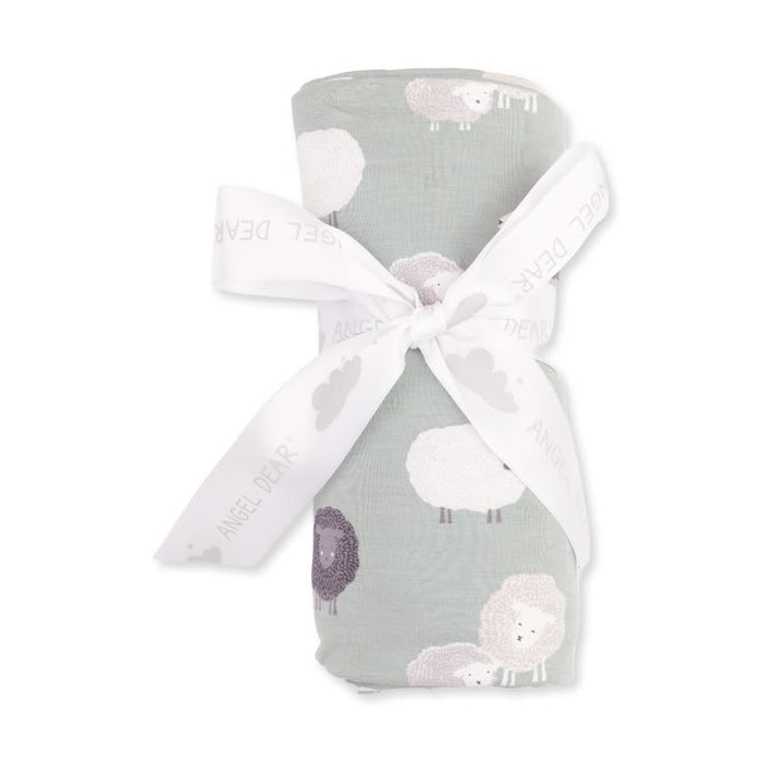 A rolled baby swaddle blanket with a sheep pattern in sage green, white, and lavender, tied with a white ribbon printed with the brand name 'Angel Dear'.