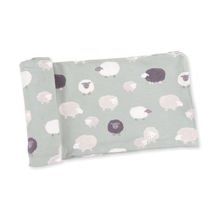 A folded baby blanket or swaddle with a repeating pattern of cute sheep in white, light gray, and dark charcoal on a muted sage green background, shown on a clean white studio background.