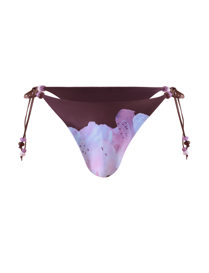 The FINLEA Bikini Bottom by TIGERMIST features beaded side tie strings and a purple-pink floral design on white for a playful look.