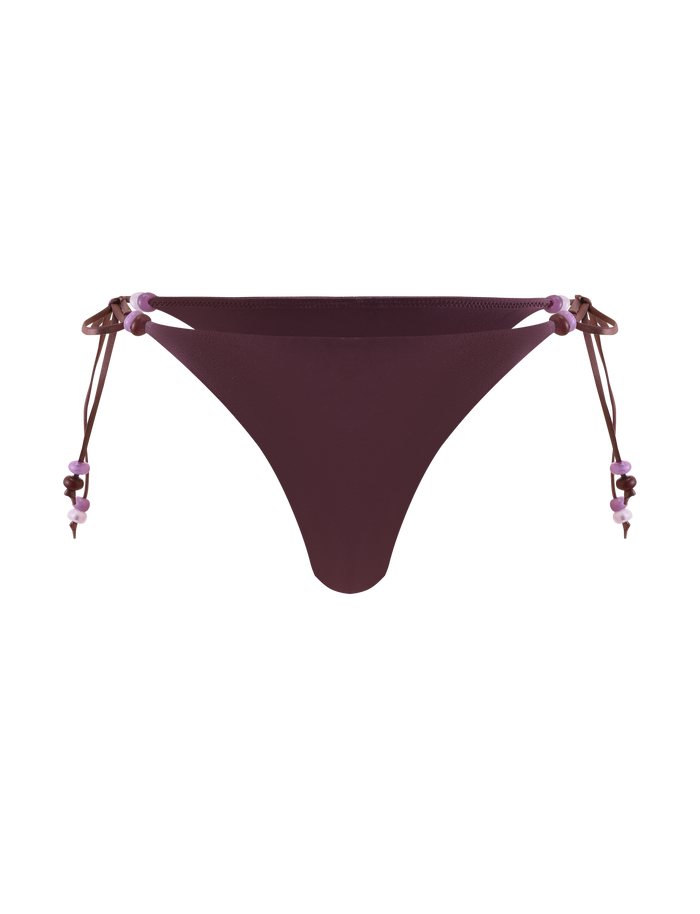 The FINLEA BIKINI BOTTOM - ZEN FLORAL by TIGERMIST features a cheeky cut in dark purple, with adjustable beaded straps embellished with small purple and pink beads, shown against a plain white background.