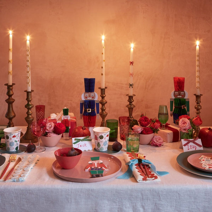 Decorative table setting with candles, plates, and small figurines on a warm-toned background.