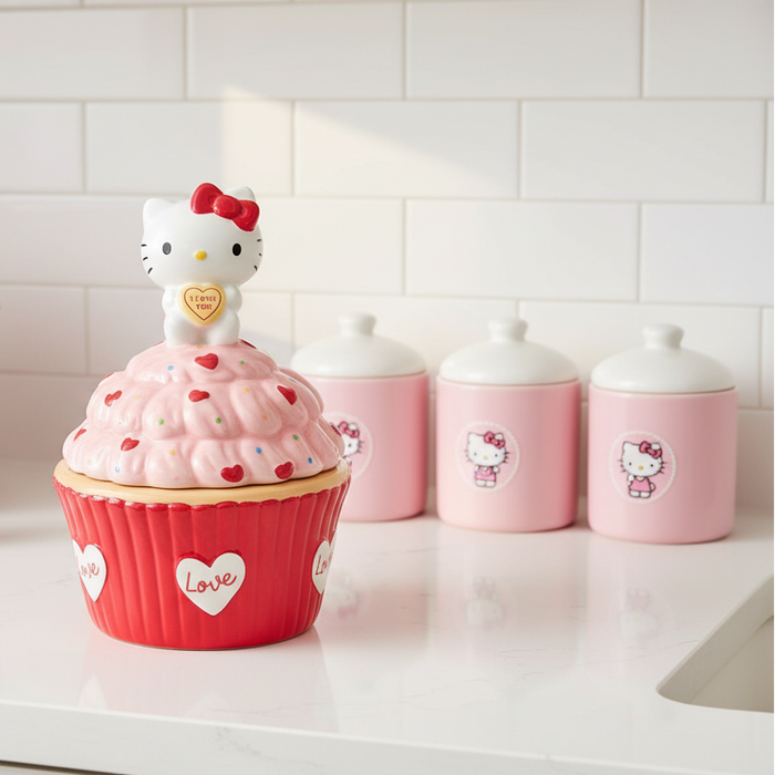 A pink Hello Kitty cupcake-shaped container sits on a white kitchen counter, styled with a matching pink Hello Kitty toaster, pink canisters, and small Hello Kitty figurines in the background.