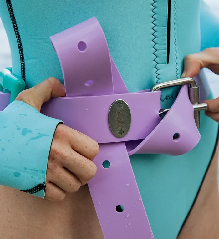 Close-up of hands fastening a purple rubber Manatee Moon weight belt with a stainless steel buckle worn over a teal wetsuit.