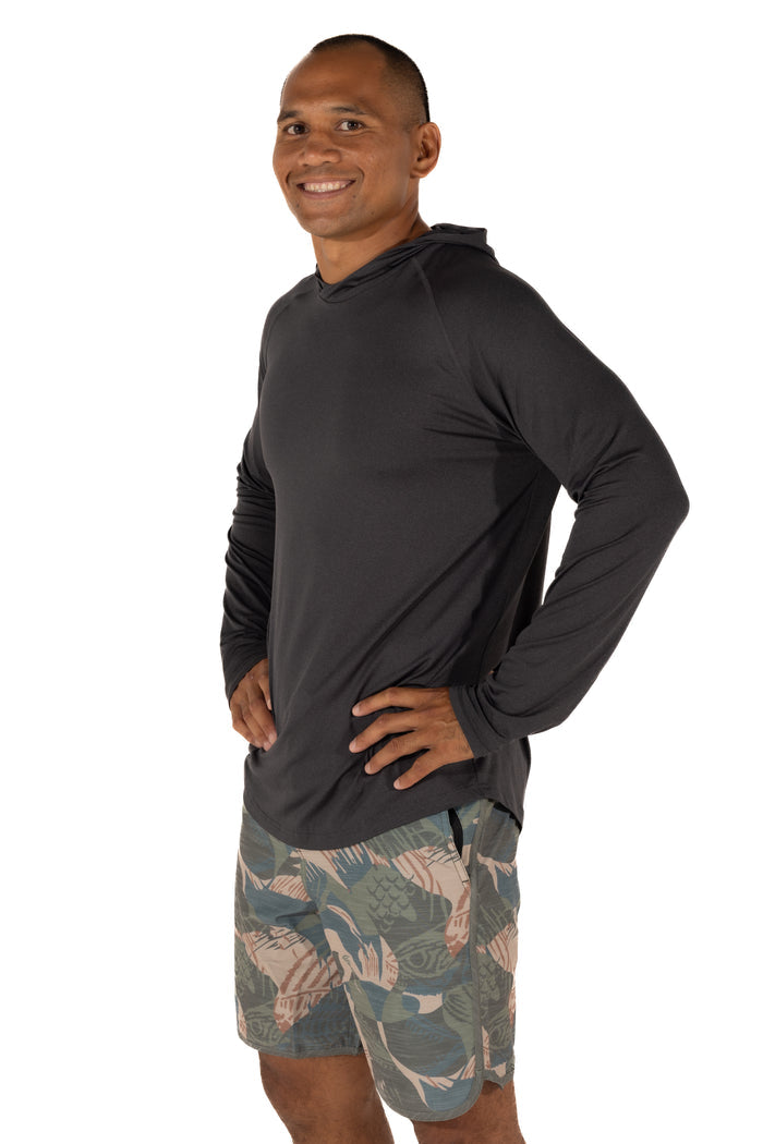 Male model wearing the Waihana Mariner Black Hooded Long Sleeve sun shirt paired with fish-print board shorts, shown from a three-quarter side angle against a white background.