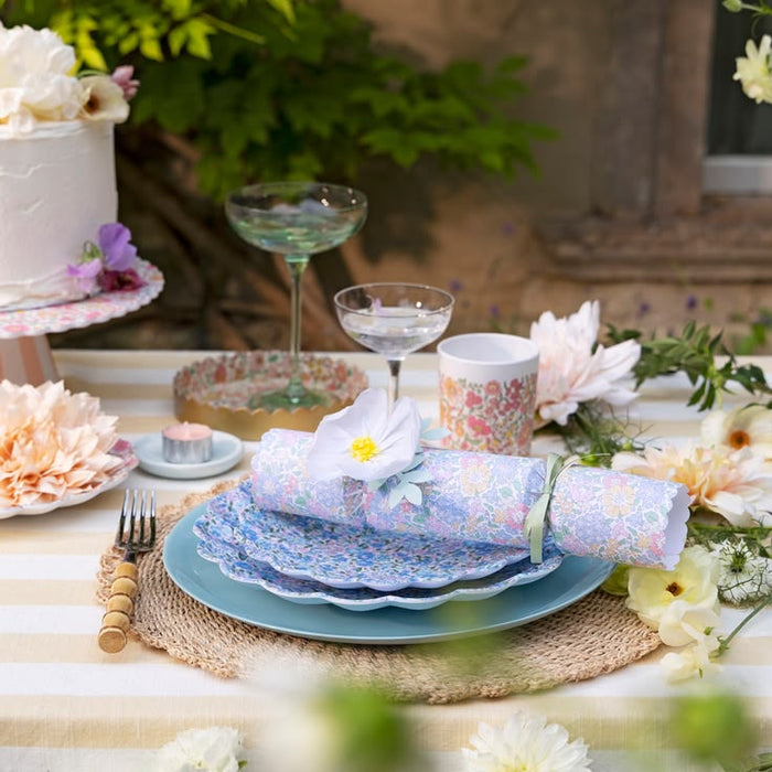 Elegant table setting with floral plates, napkins, and glasses on a table outdoors.