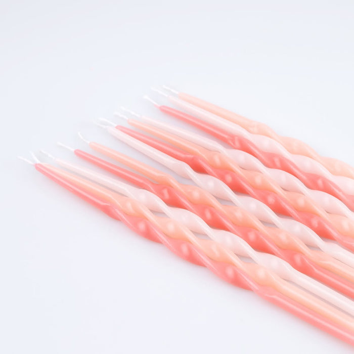 A set of twisted taper candles in a soft pink and peach gradient, arranged diagonally on a clean white background.