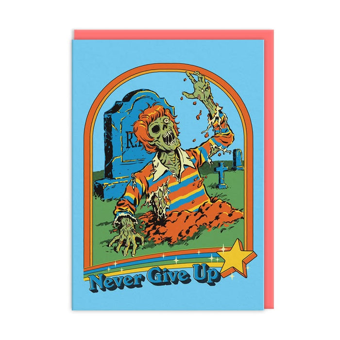 A square greeting card with a light blue front featuring a cartoon zombie rising from a graveyard and the words 'Never Give Up' at the bottom, shown with a pink envelope behind it on a white background.