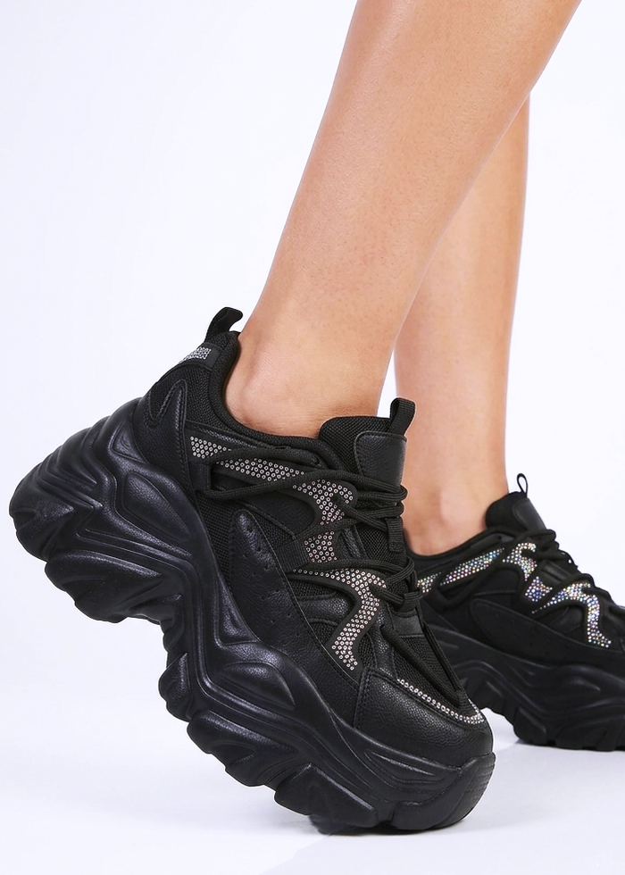 On-model studio view of Berness Nikki Black Platform Sneakers showcasing the thick silhouette and reflective rhinestone accents in motion.