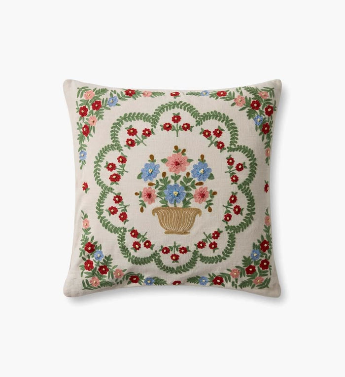 A square decorative throw pillow with a cream-colored linen background, featuring a central embroidered floral bouquet in a basket surrounded by a green leafy wreath and red, pink, and blue flowers.