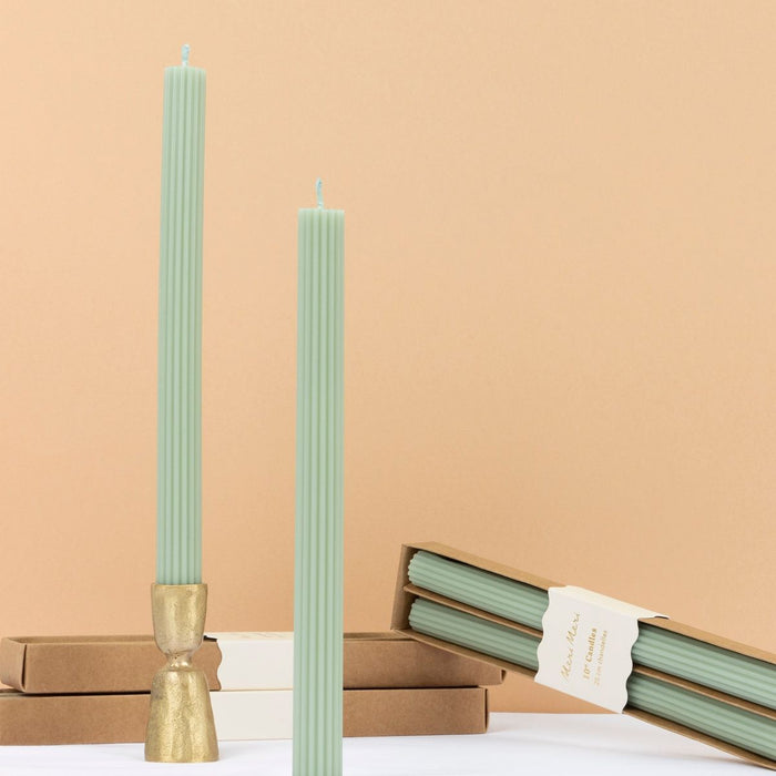 Two tall green candles with gold holders on a beige background