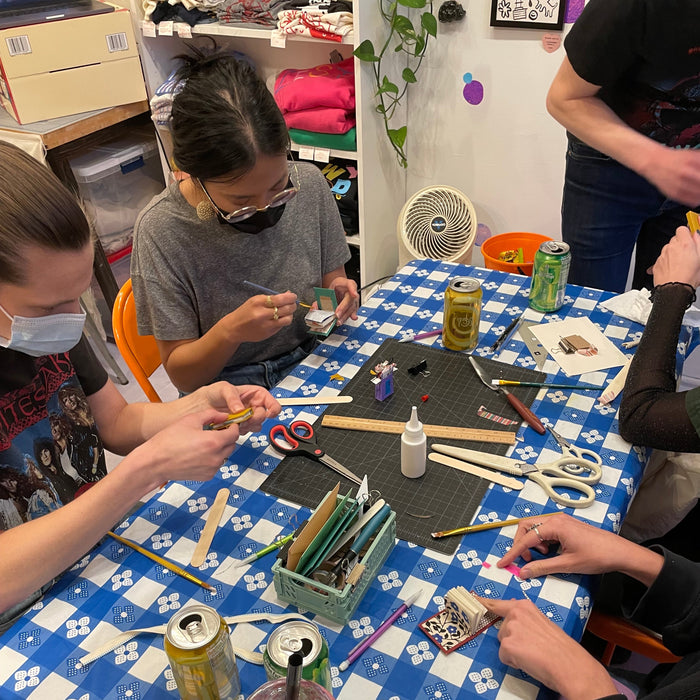 Top-down view of a table with various bookmaking supplies and people around it putting together tiny books.