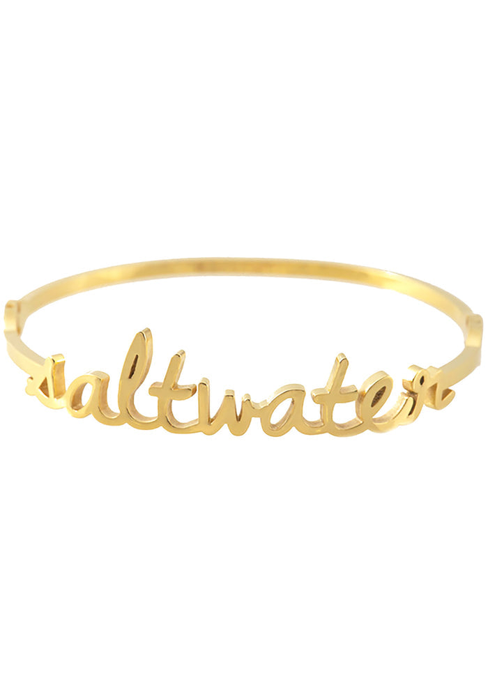 Wanderlust + Co Saltwater Bangle in gold with cursive saltwater script on 24k plated stainless steel hinged bangle bracelet — front view